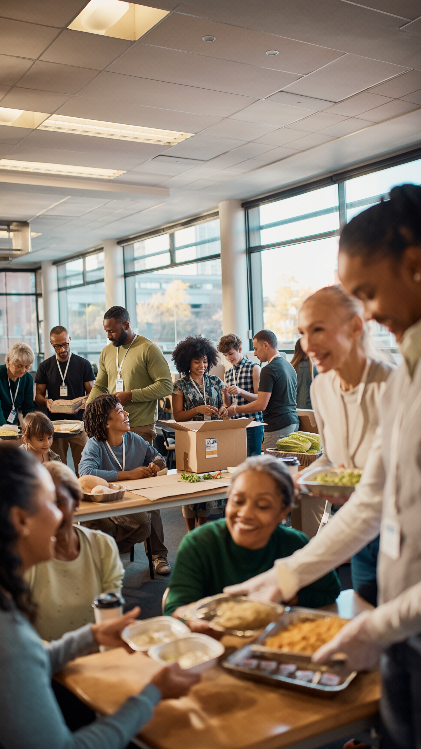 800x800 Diverse volunteers and community members gather in a bright, welcoming indoor space to share nutritious meals with dignity and respect. Multi-generational families connect over food distribution at a Boston community center, demonstrating Teranga Grill's mission to combat food insecurity through empowerment rather than charity. Professional volunteers of different ages and backgrounds collaborate to serve fresh meals while fostering genuine relationships and community belonging. Strength-based food access program emphasizing hope, connection, and sustainable food solutions in Nubian Square, Boston.